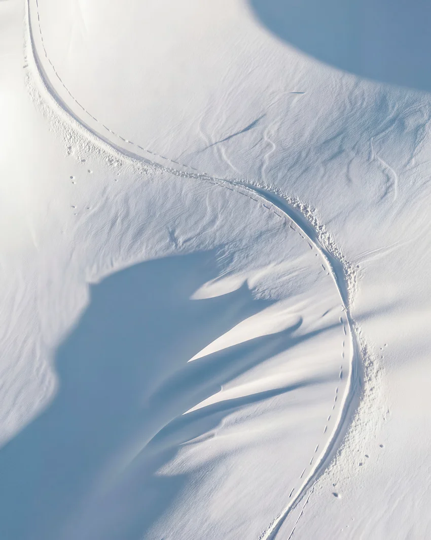 Aerial view of wind-sculpted snow ridges and ski tracks curving across an alpine slope for Dom Pérignon — 3d product visualization Detroit, photography & art direction by Pierrick Jégou, produced by Detroit AI Production House