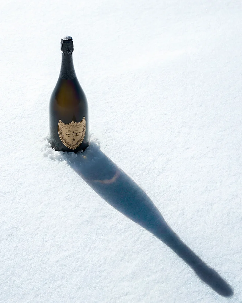 Dom Pérignon bottle standing upright in fresh snow, casting a long diagonal shadow under bright sunlight — 3d product animation Detroit, photography & art direction by Pierrick Jégou, produced by Detroit AI Production House