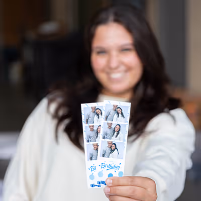 Vrouw lacht en toont twee fotostrips met verjaardagsfoto's en blauwe feestdecoraties.