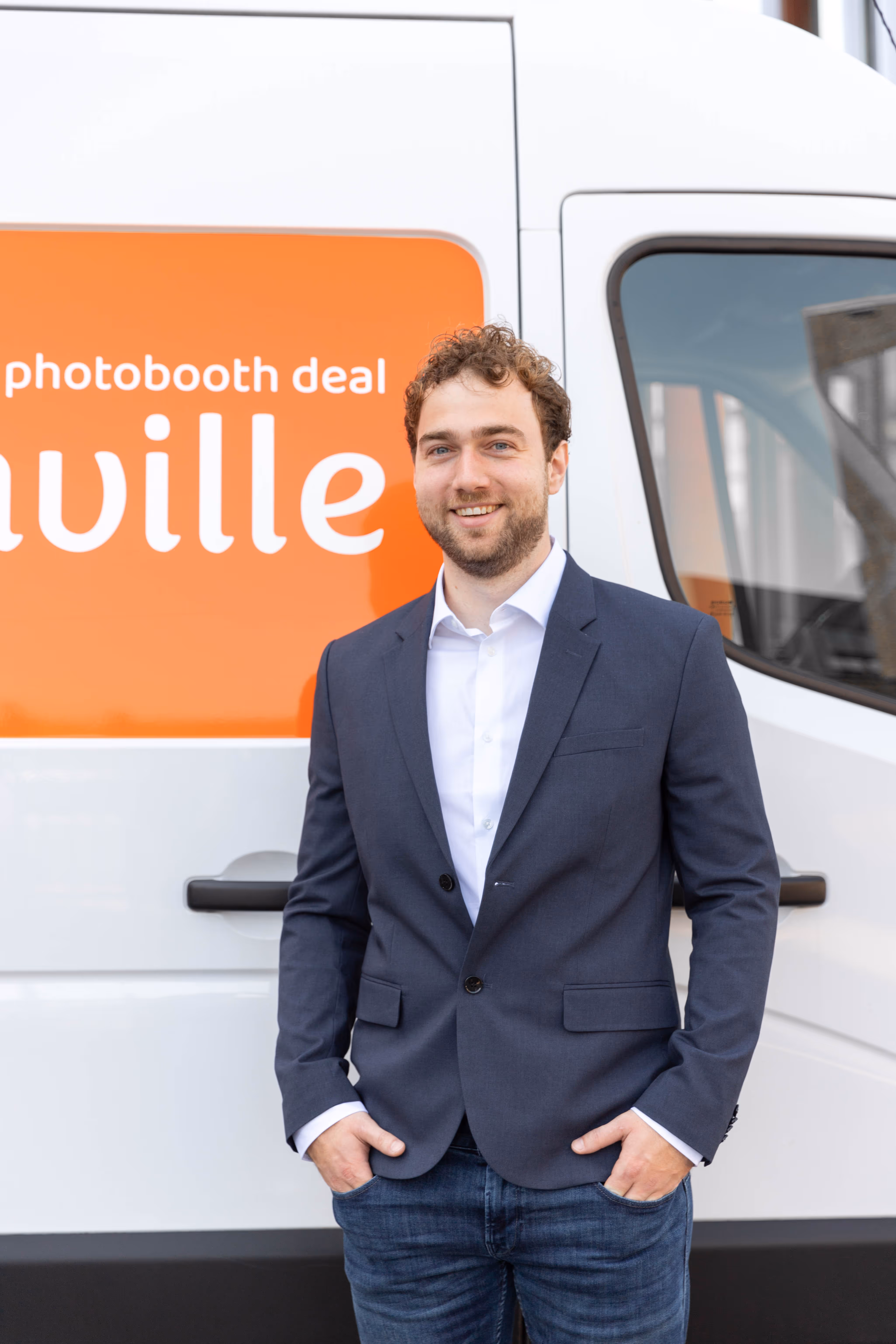 Directeur van Boothville staat met blauwe blazer en witte overhemd voor een Boothville bestelauto.