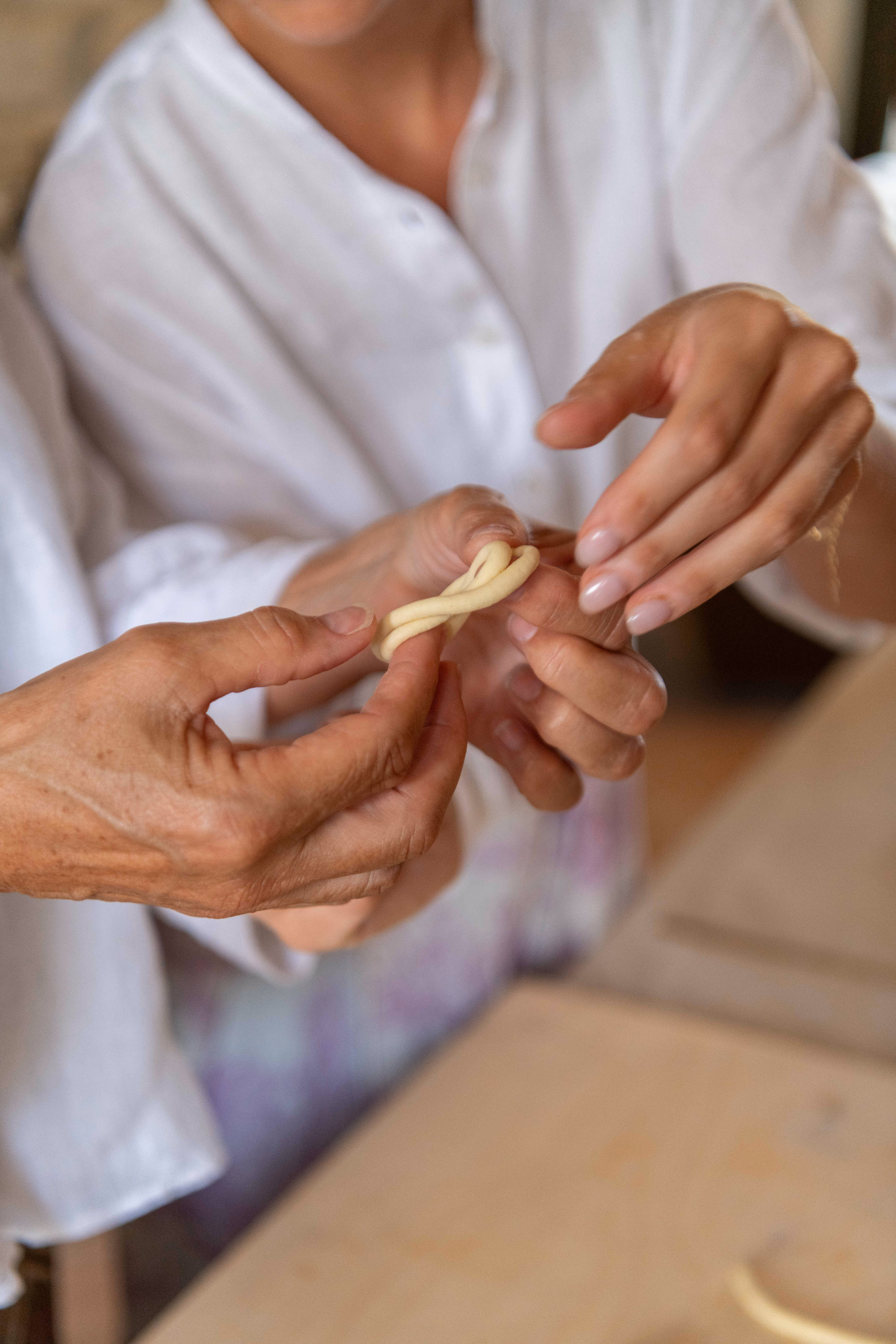 Due persone che lavorano insieme a modellare un piccolo intreccio di pasta fresca con le mani.