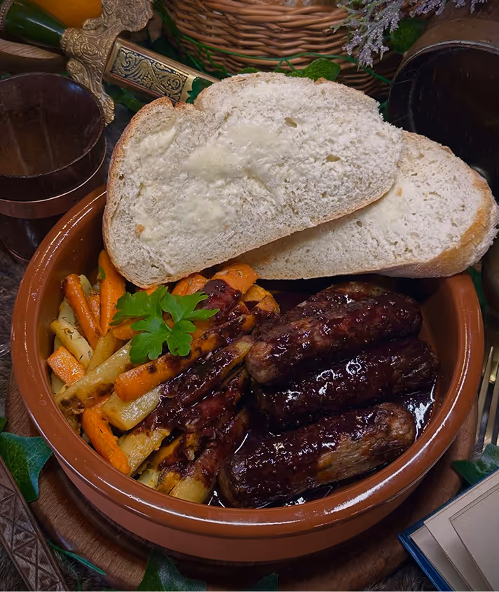 Clay bowl with grilled sausages, roasted carrots and parsnips, garnished with parsley, topped with two slices of buttered bread.