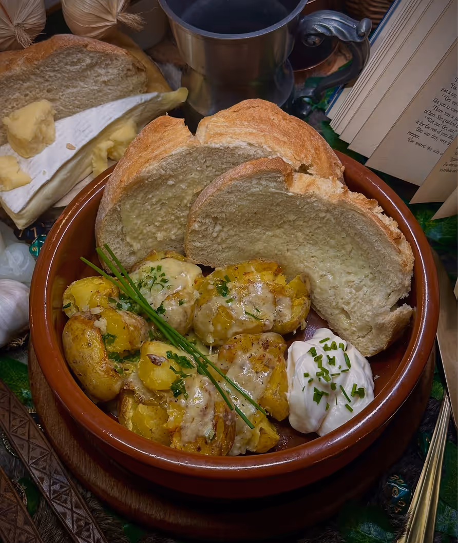 Bowl with smashed roasted potatoes garnished with chives, two slices of rustic bread, and a dollop of sour cream topped with chopped chives.