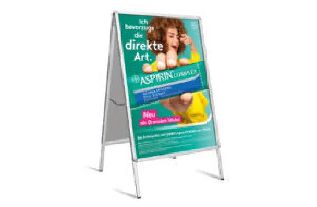Aufsteller mit Werbung für Aspirin Complex, zeigt eine Frau mit gelbem Pullover, die direkt auf den Betrachter zeigt.
