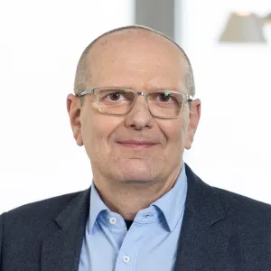 Porträt von Jörg Barnhusen mit Brille, blauem Hemd und dunklem Sakko vor hellem Hintergrund.