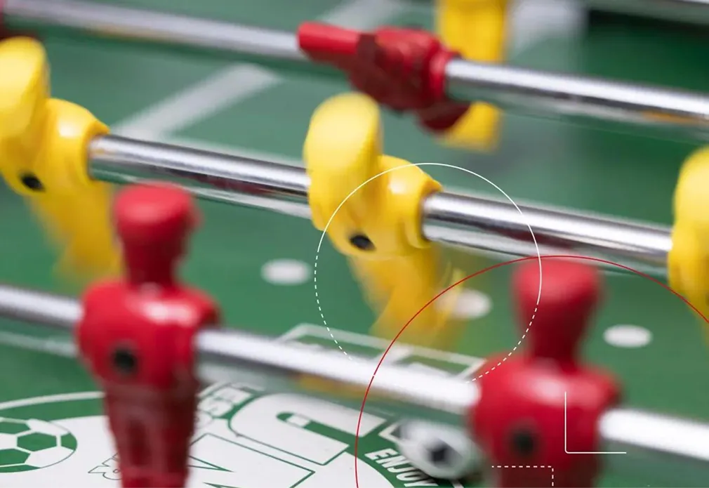 Nahaufnahme eines Kicker-Tischspiels mit roten und gelben Spielfiguren auf grüner Spielfläche.