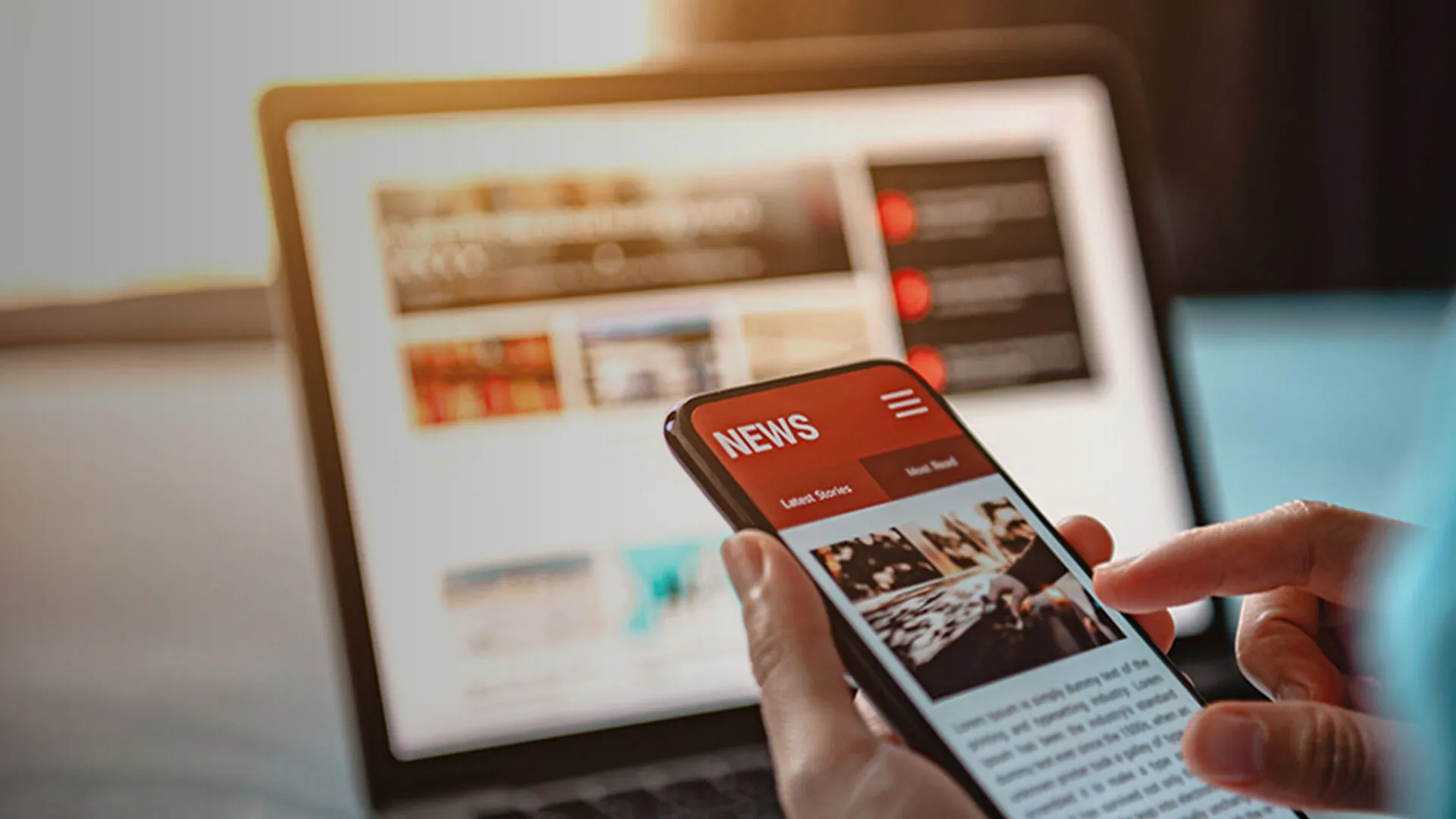 Eine Person hält ein Smartphone mit einer Nachrichten-App, im Hintergrund ein verschwommener Laptopbildschirm mit weiteren Nachrichten.