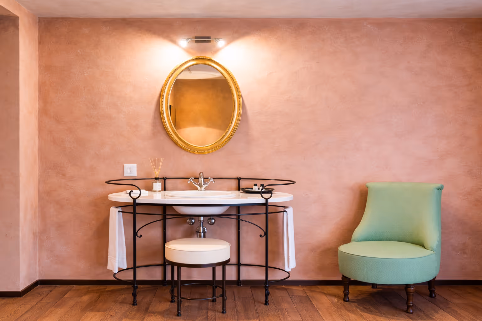 Raffinato angolo lavabo in stile classico all'interno della Camera Unique, affiancato da una poltroncina verde pastello in contrasto con le pareti color terracotta.