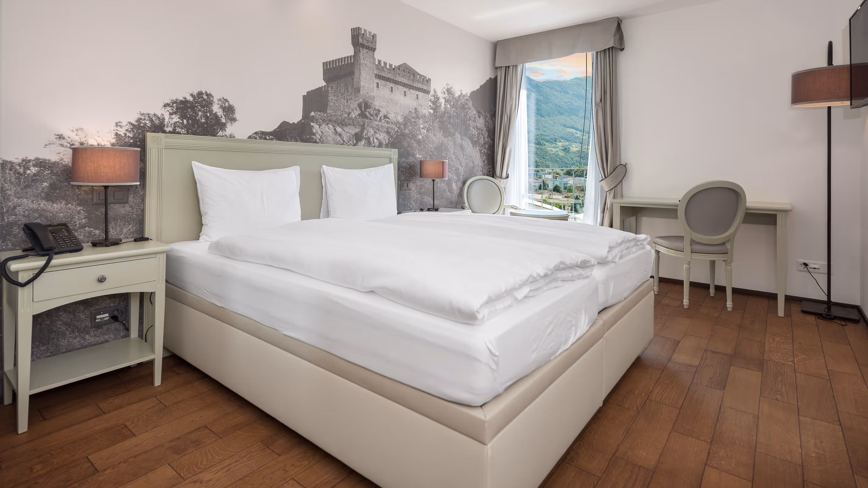 Grande chambre double lumineuse à l'Hotel La Tureta avec murale des châteaux de Bellinzone, parquet et vue panoramique.
