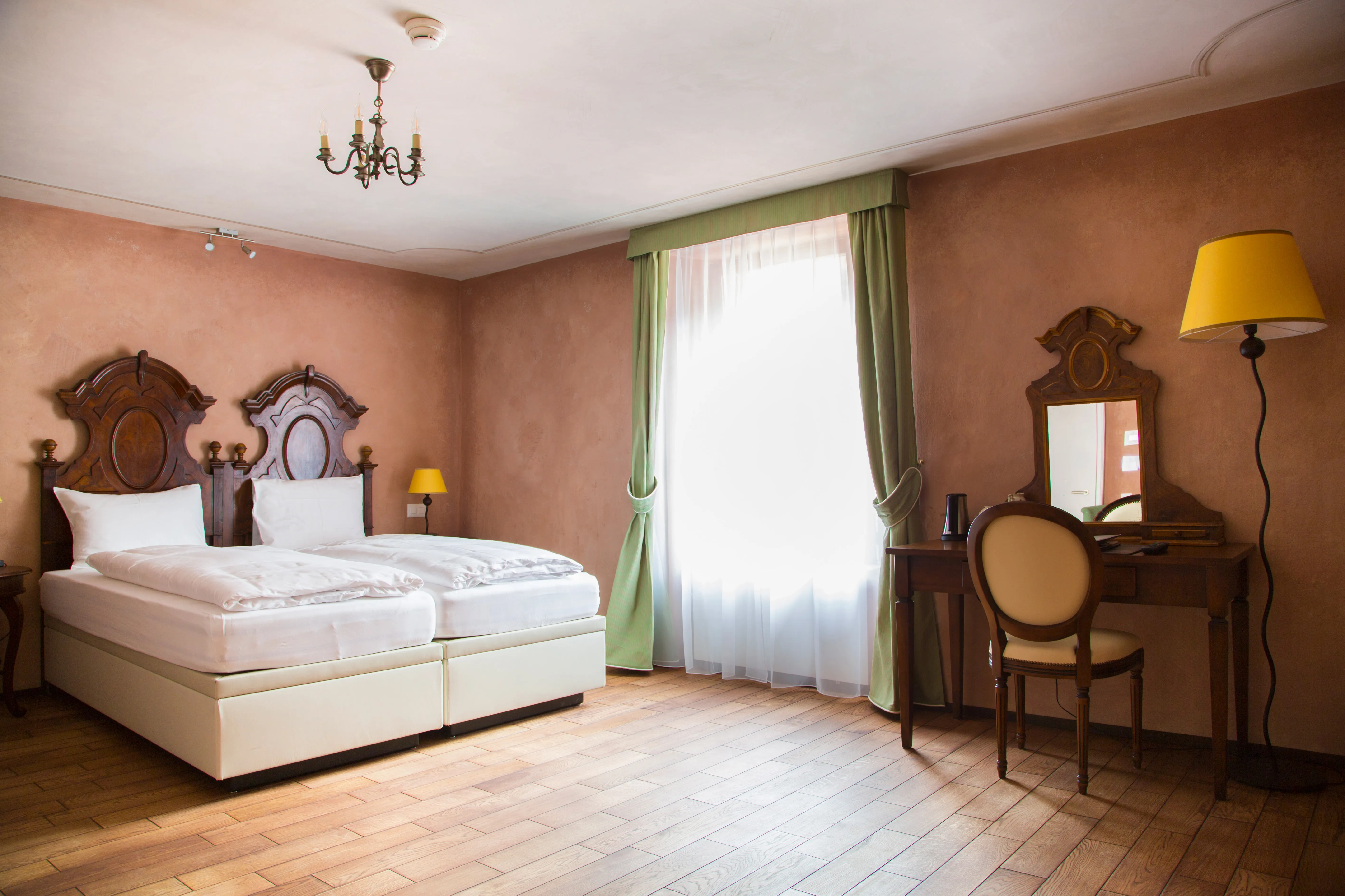 Spaziosa Camera Unique a Bellinzona, che unisce comfort moderno e arredi d'epoca, tra cui letti con testiere storiche e uno scrittoio classico vicino alla finestra.