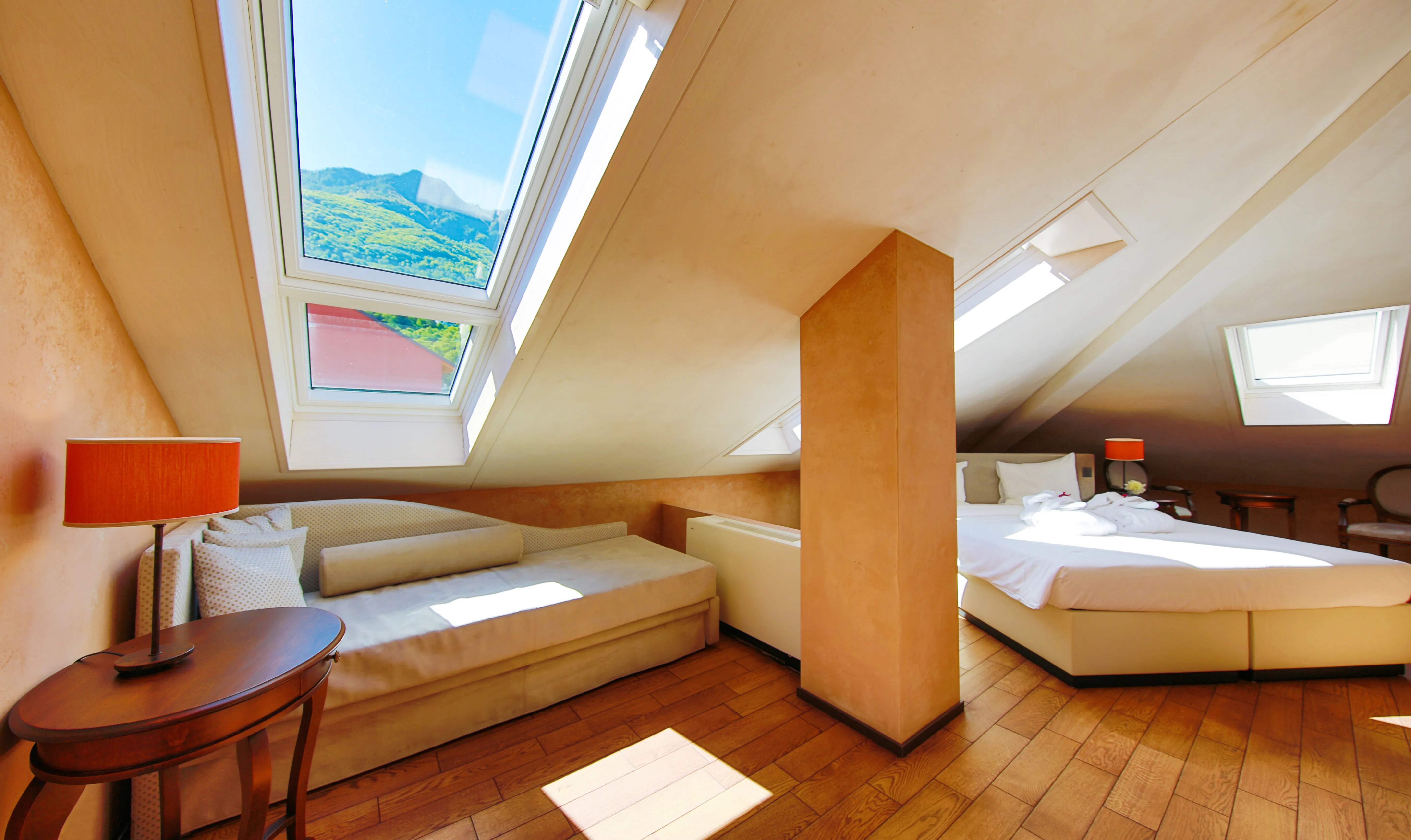 Spazioso open space del Junior Loft sotto il tetto spiovente: a sinistra un'accogliente zona relax con divano, a destra la zona notte, entrambe illuminate da ampi lucernari con vista.