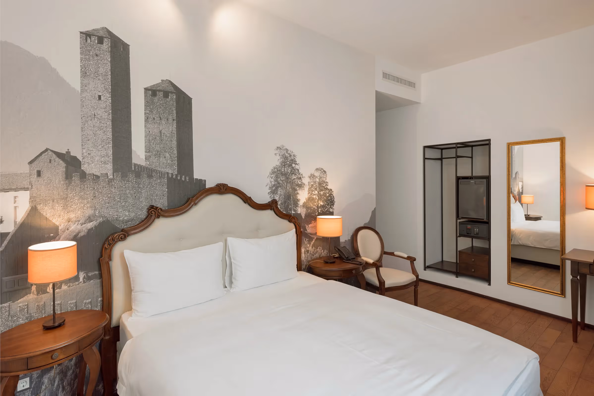 Chambre Cosy Queen : lit double, fauteuil classique capitonné et armoire ouverte avec minibar et coffre-fort.