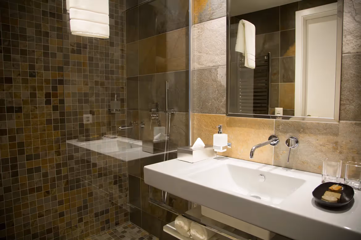 Zona doccia e lavabo: Bagno moderno con doccia a filo pavimento, rivestimento in piastrelle di pietra e lavabo bianco con set di cortesia e asciugamani.
