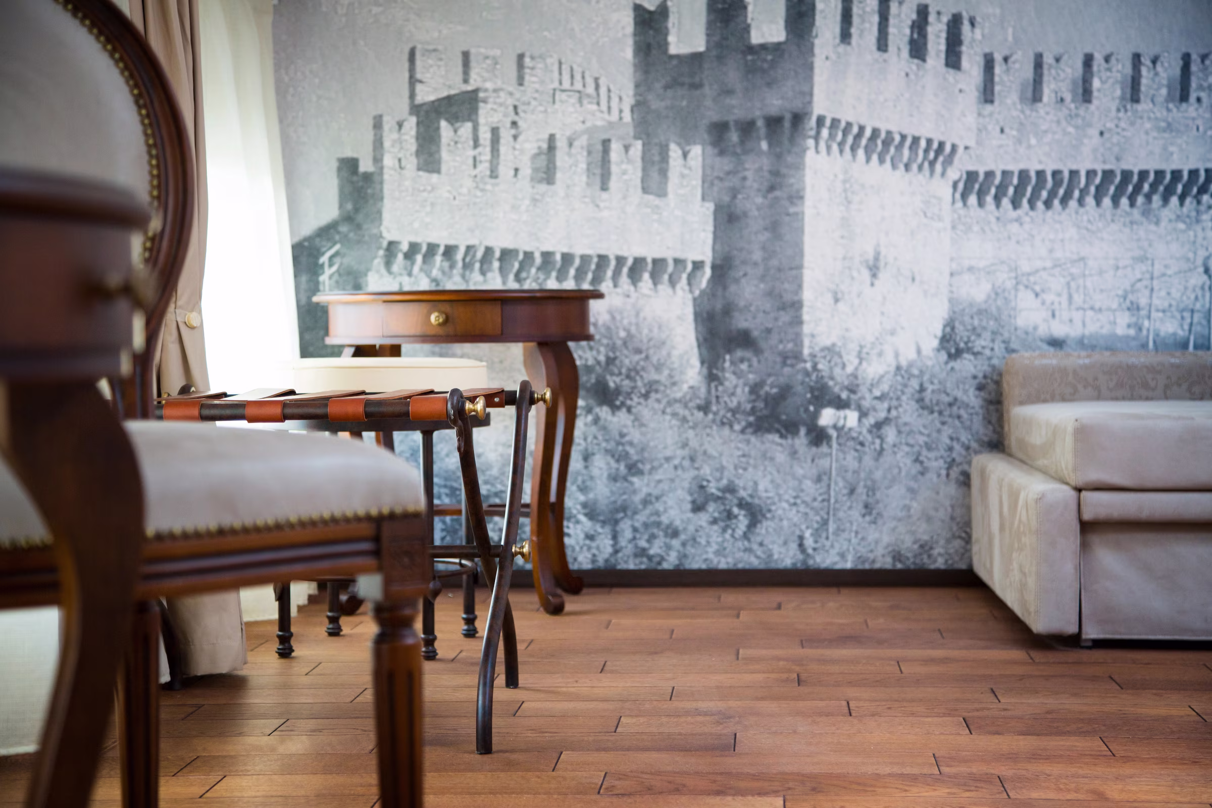Carta da parati fotografica con le mura medievali di Bellinzona, integrata armoniosamente con sedie classiche e portavaligie in pelle.