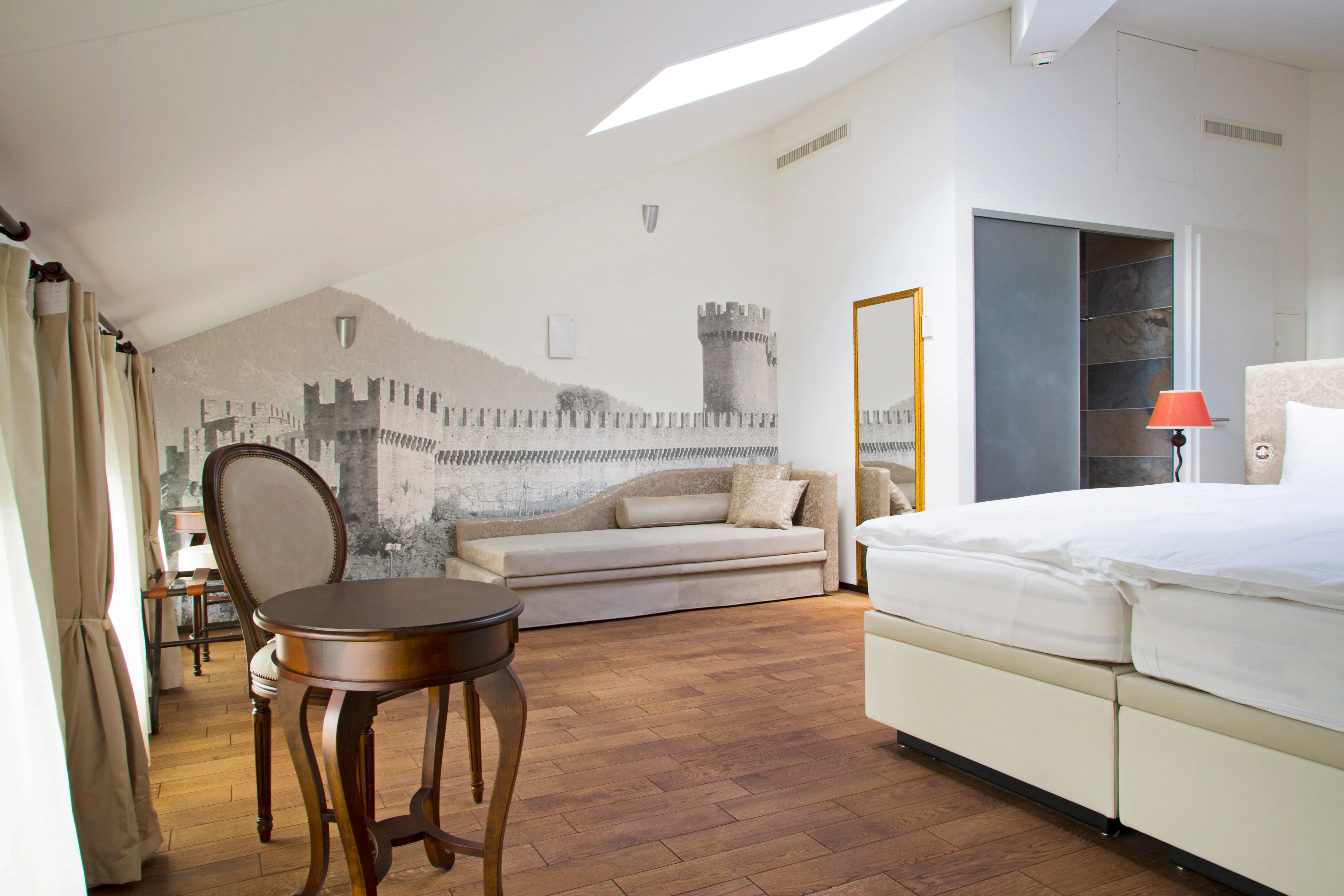 Zona notte della camera Design Loft all'Hotel La Tureta, con letto king-size, pavimento in legno e decorazioni murali ispirate ai castelli di Bellinzona.