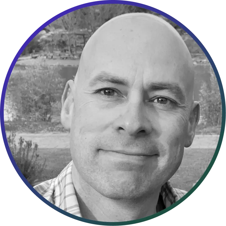 Close-up black and white portrait of a smiling bald man outdoors.