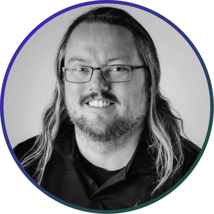 Smiling man with glasses and shoulder-length hair in a black shirt against a plain background.