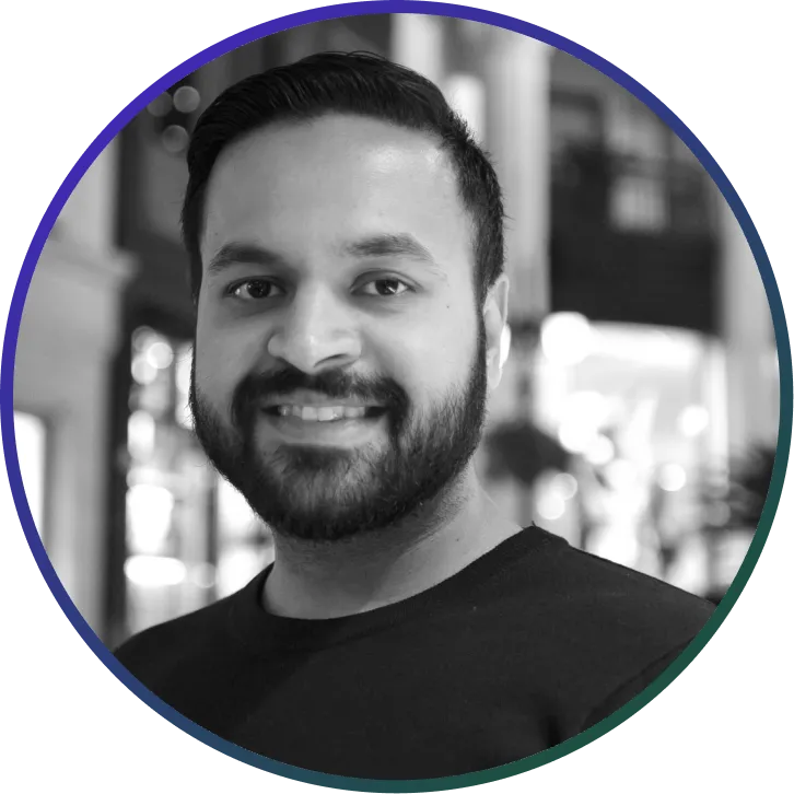 Smiling man with short dark hair and beard wearing a dark shirt with blurred indoor background.