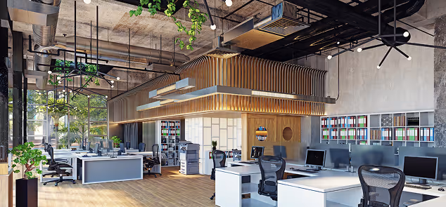 Modern open-plan office with multiple desks, ergonomic chairs, computers, green plants, and wooden accents under exposed concrete ceiling.