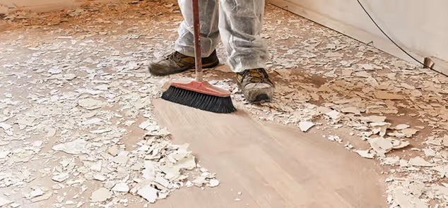 Person sweeping peeled paint and debris from a floor with a broom.