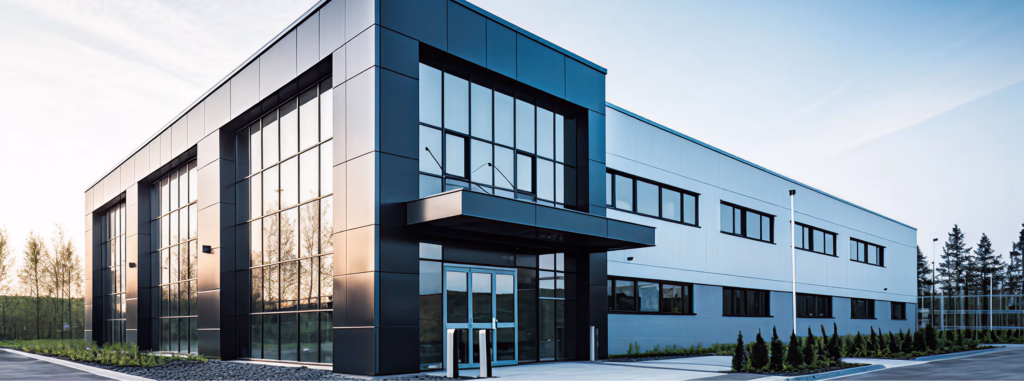 Modern commercial building with large glass windows and black and white exterior panels surrounded by landscaped greenery.