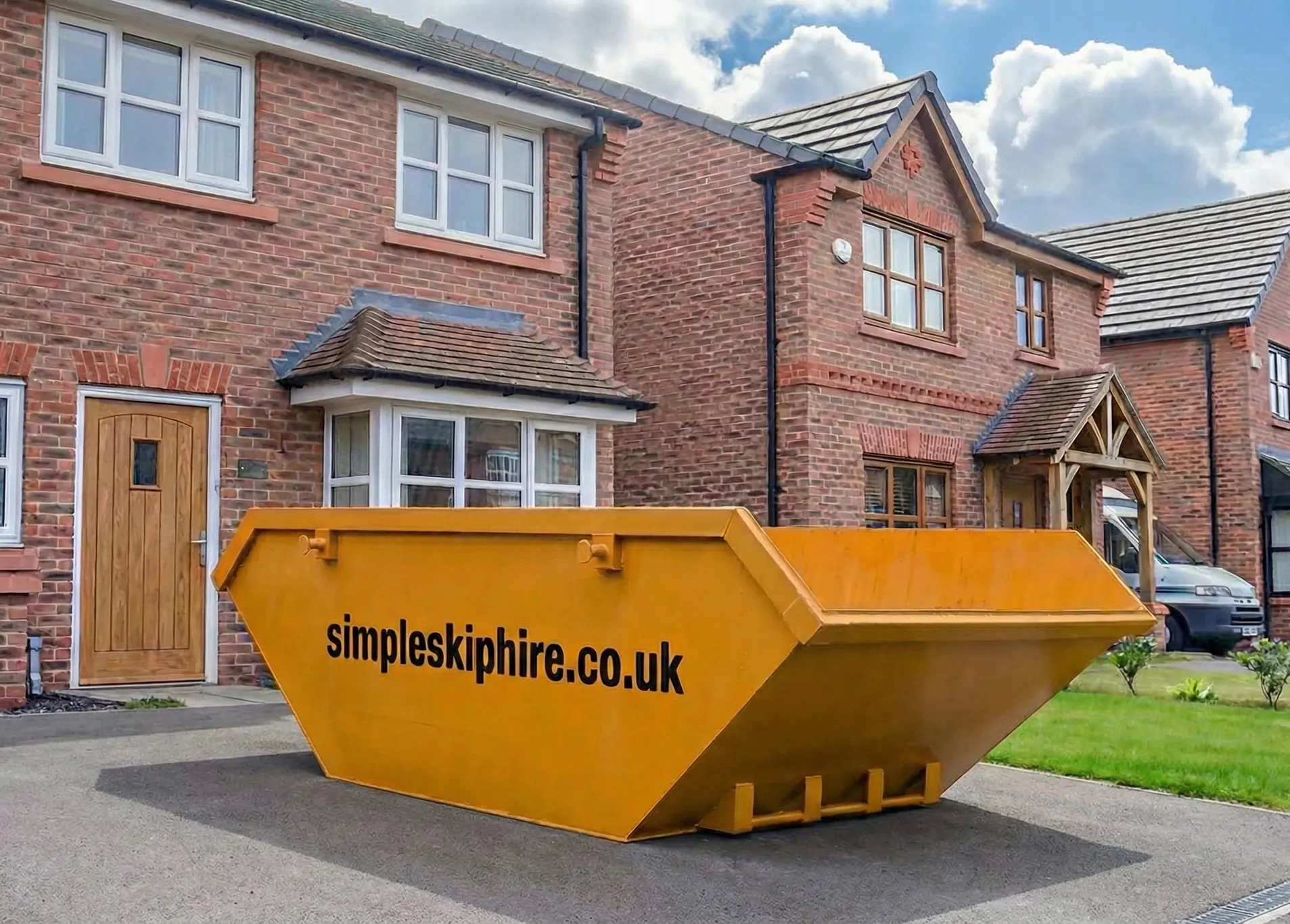 Yellow skip bin with simpleskiphire.co.uk text parked on a driveway in front of brick houses.