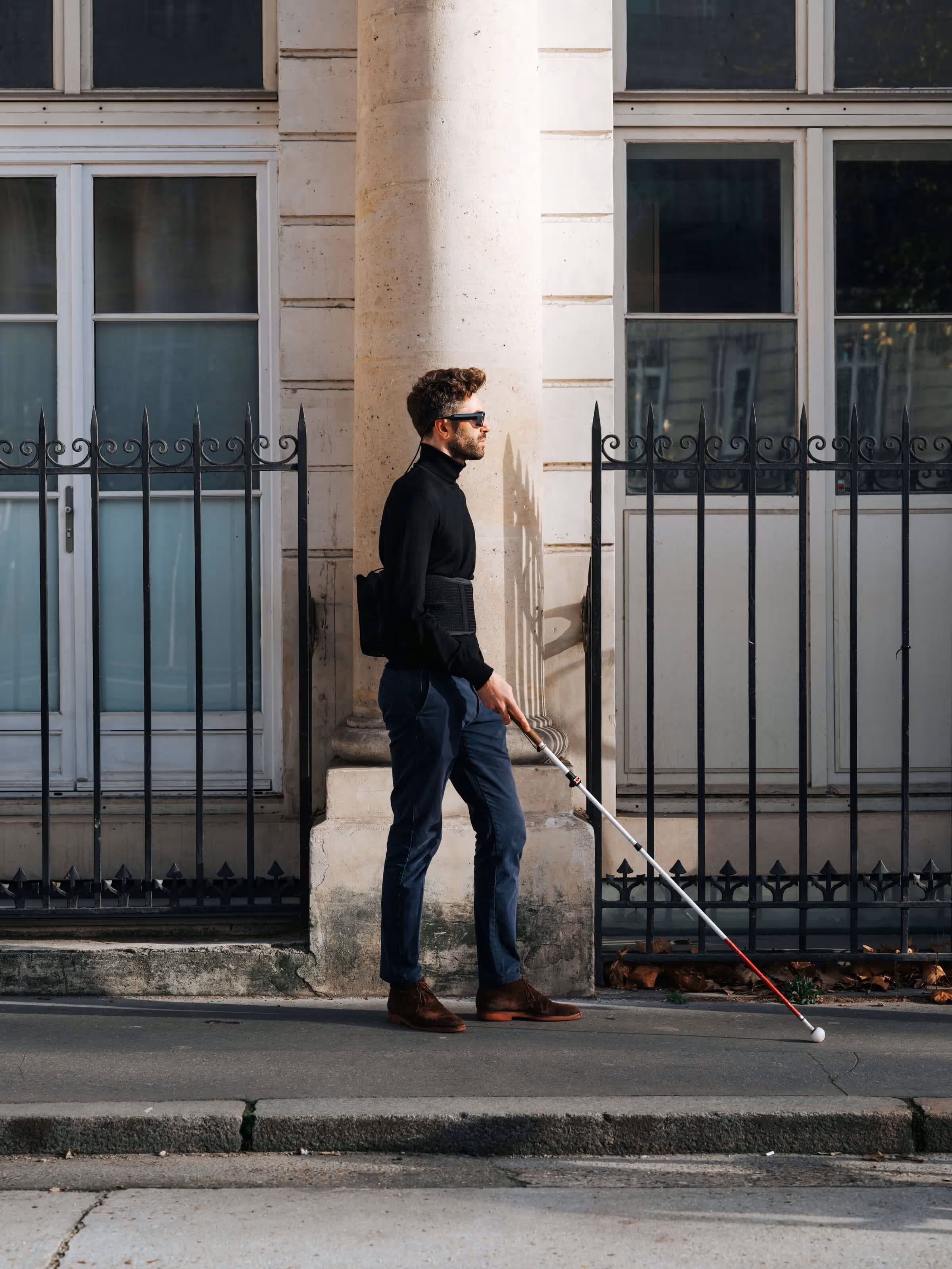 Un homme marche dans la rue équipé du dispositif et de la canne. Grâce au retour haptique, l’utilisateur perçoit son environnement au dela de la simple détection d'obstacles
