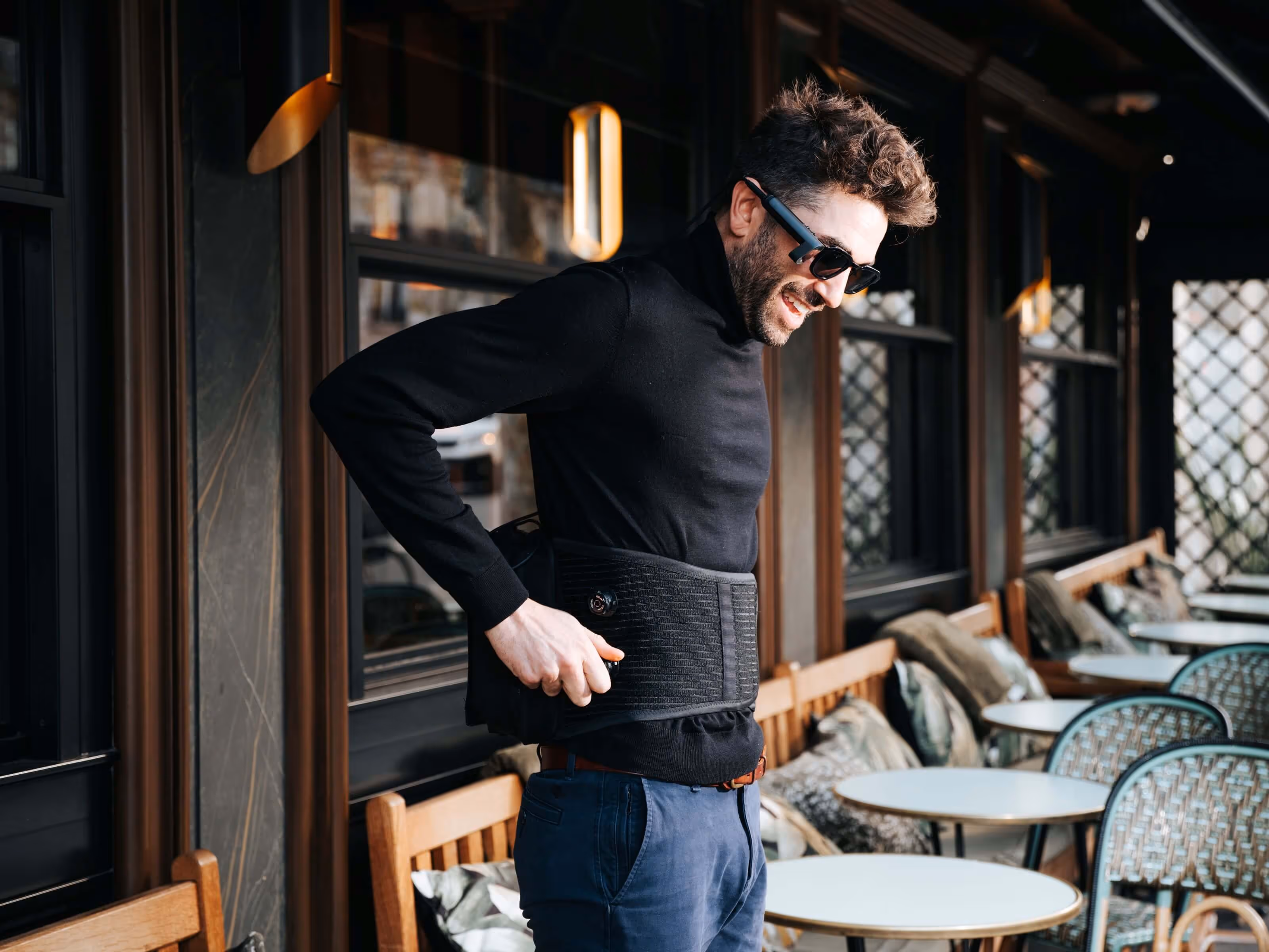 Un homme équipé du dispositif SeeHaptic se tient debout au niveau d'une terrasse de café. Il règle facilement la ceinture haptique qui s’adapte à chaque morphologie