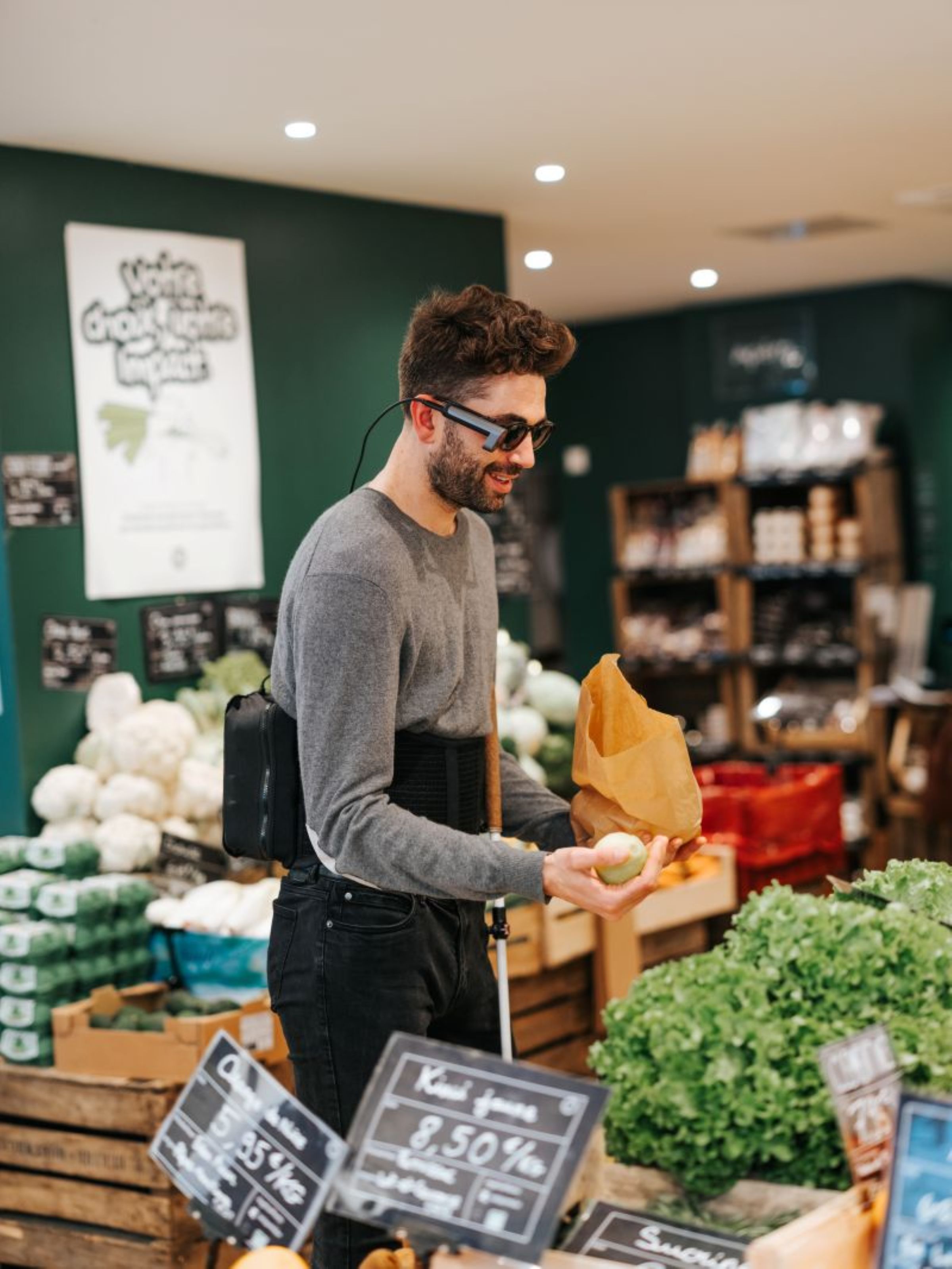 Un homme fait ses courses chez le primeur équipé du dispositif SeeHaptic qui lui permet de percevoir les éléments autour de lui et d'avoir les informations via l'assistant vocal.