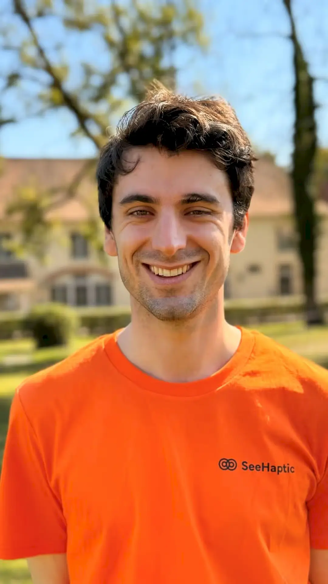 Rémi du Chalard, fondateur et inventeur de SeeHaptic, se tient debout et souriant. Il porte un t shirt orange SeeHaptic.