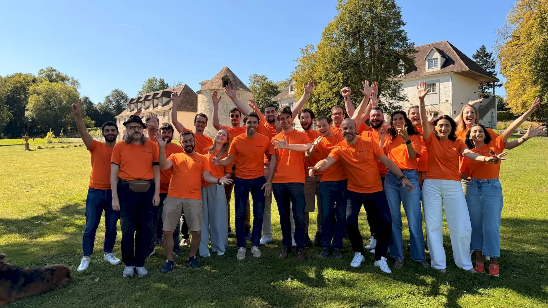 L’équipe SeeHaptic réunissant ingénieurs, designers et experts de l'accès marché. L'équipe se tient debout les bras levés en signe d'entousiasme. Ils portent tous des t shirts oranges SeeHaptic.