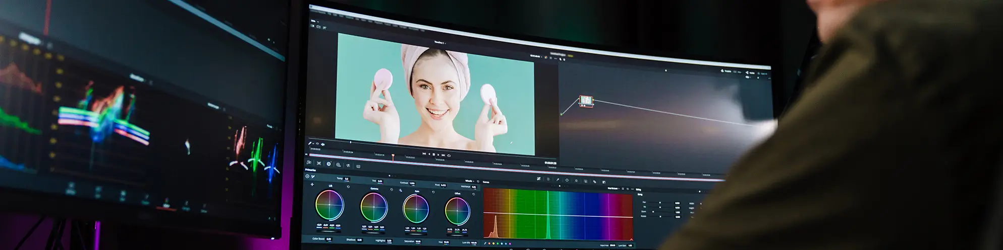 Rückansicht eines jungen Mannes, der an einem Arbeitsplatz Videoschnitt mit Farbkorrektursoftware durchführt.