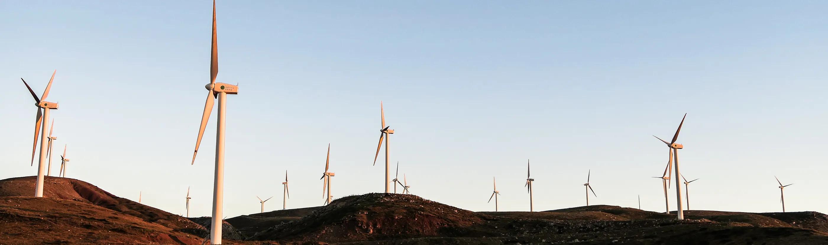 Wind turbines across rolling hills under a clear blue sky at sunset.