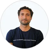 Smiling man with curly hair and a beard wearing a navy blue t-shirt.
