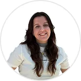 Smiling woman with long dark hair wearing a white top and standing against a white background.
