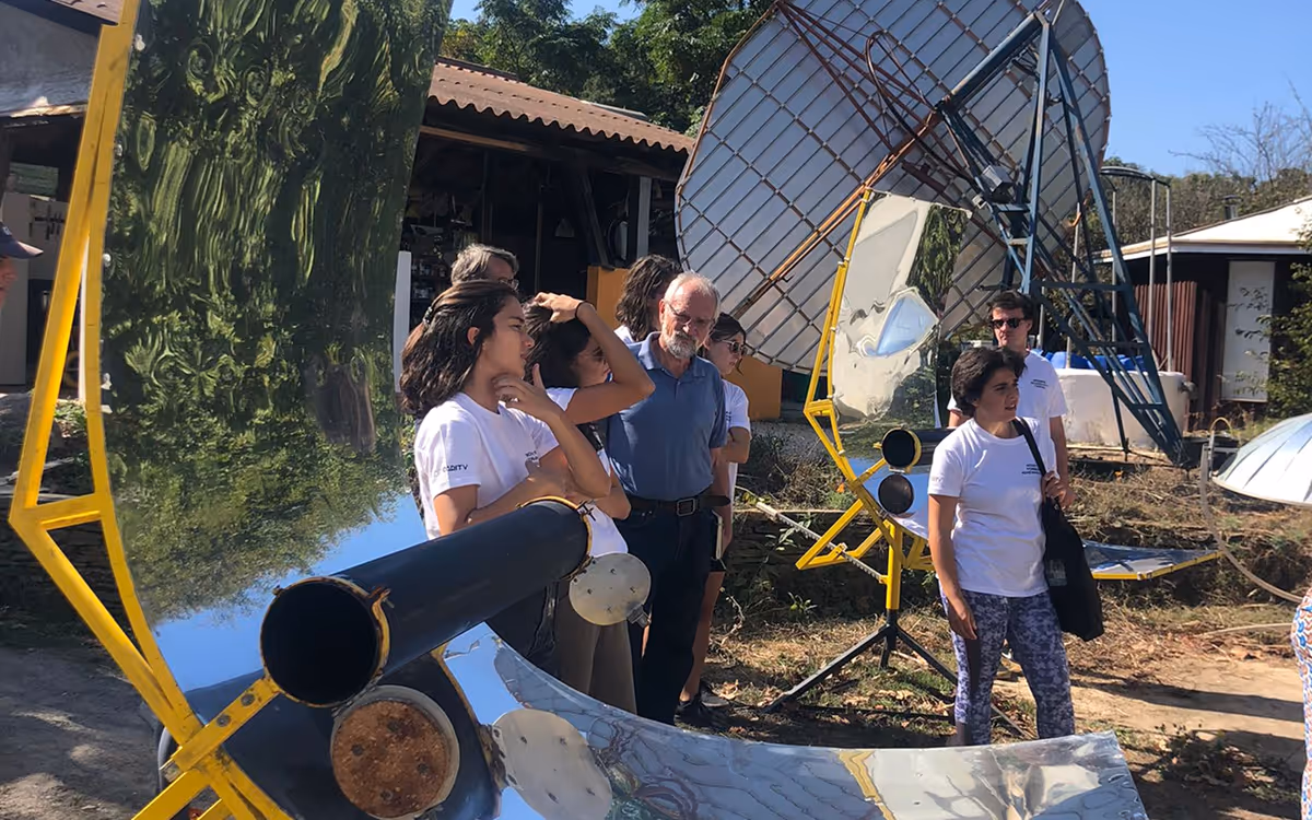 Group around solar cooker prototypes with reflective panels outdoors on a sunny day.