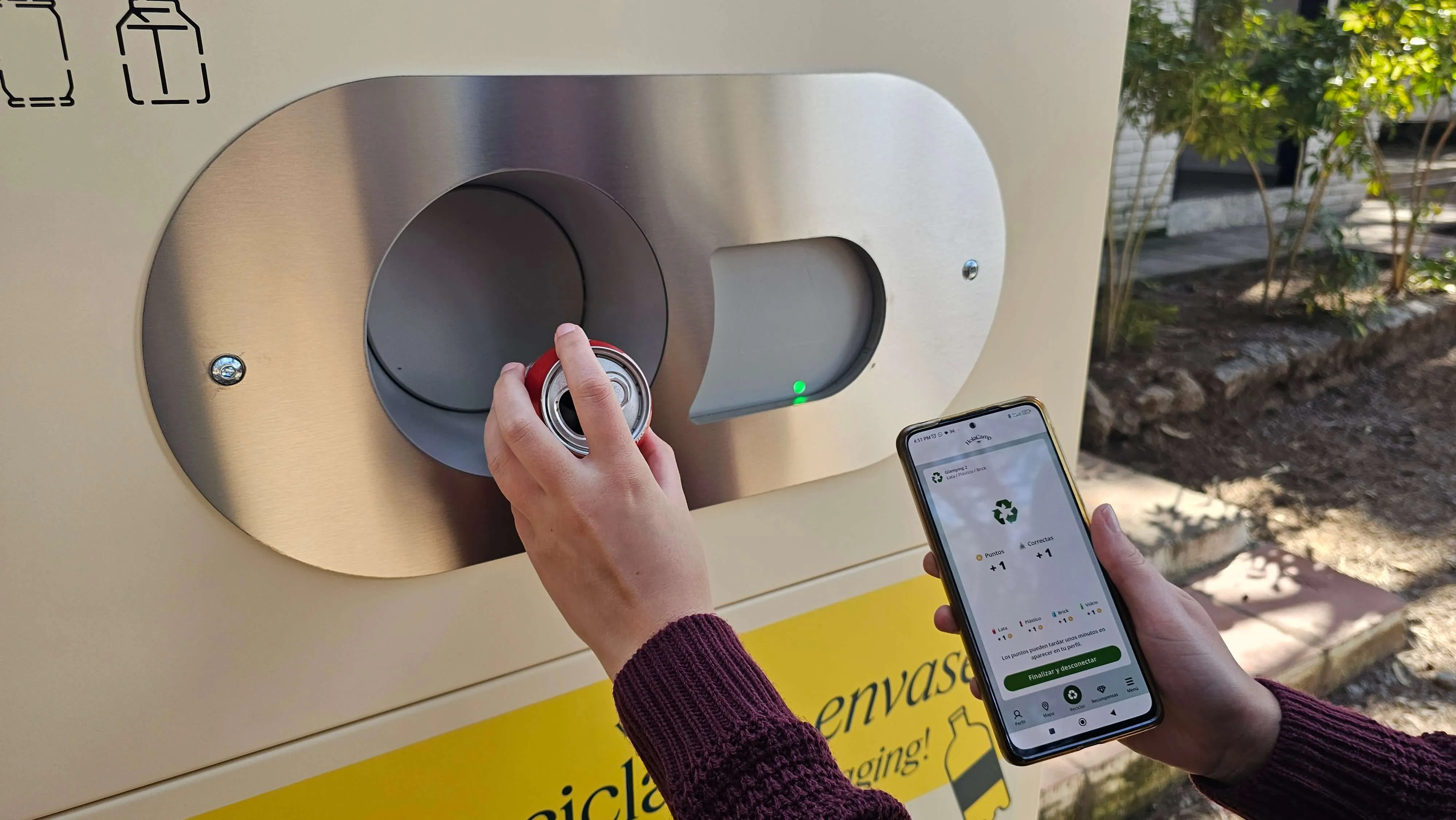 Person inserting a can into a recycling machine while holding a phone showing recycling points.