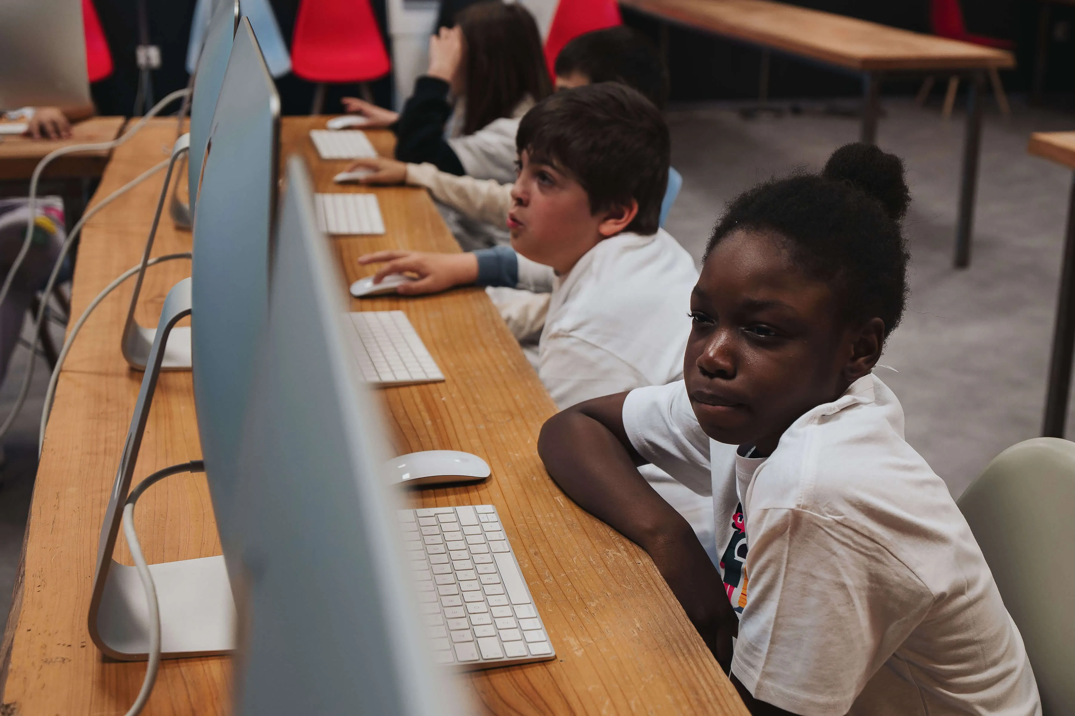 Children sitting at desktop computers in a classroom, focused on their screens and work.