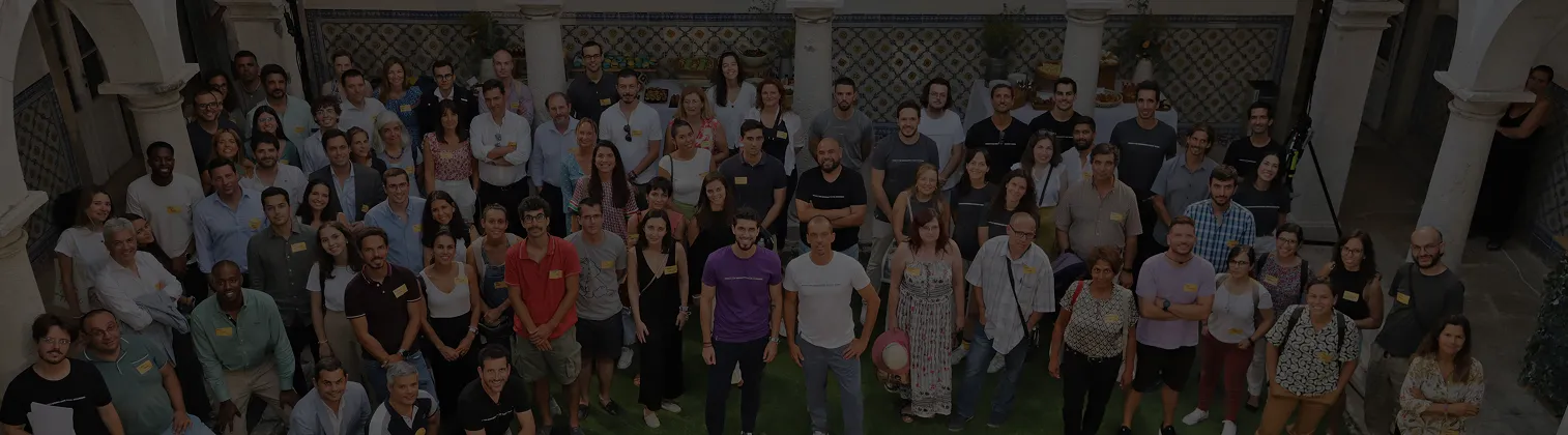 Large group of diverse adults standing closely together in a courtyard with tiled walls and stone columns.