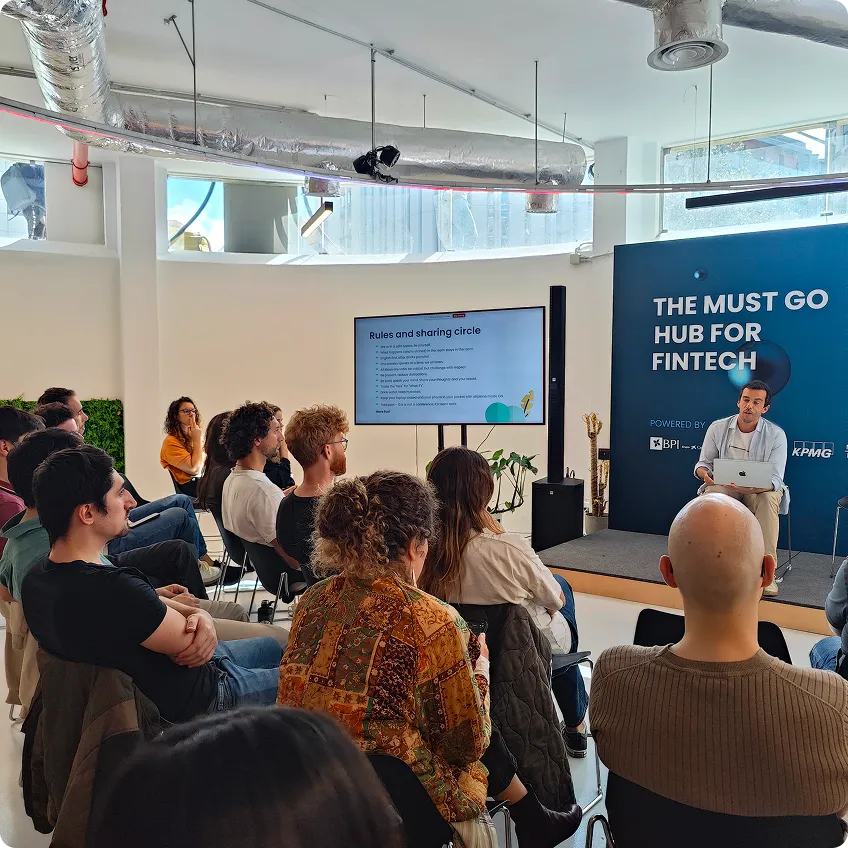 Group attending a fintech presentation with speaker on stage and rules displayed on screen.