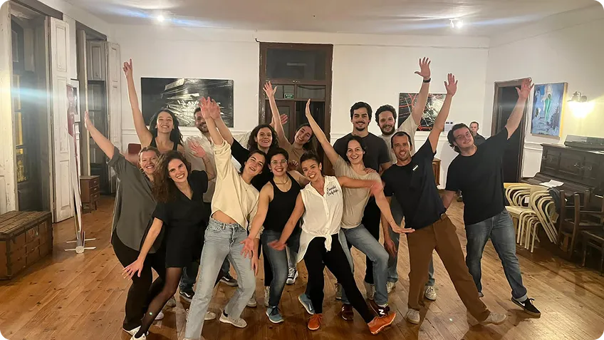 Group of smiling people posing happily indoors with arms raised and wooden floor.