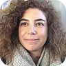 Headshot of a woman with curly hair smiling slightly against a pale background.