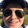 Person wearing black sunglasses and a dark cap smiling outdoors.