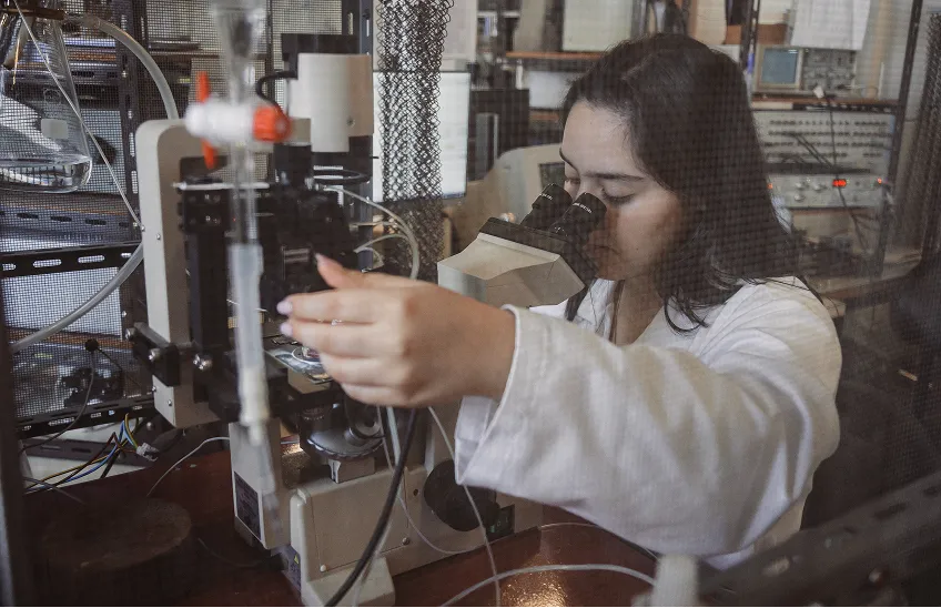 Female scientist in lab coat using a microscope and adjusting equipment in a laboratory.