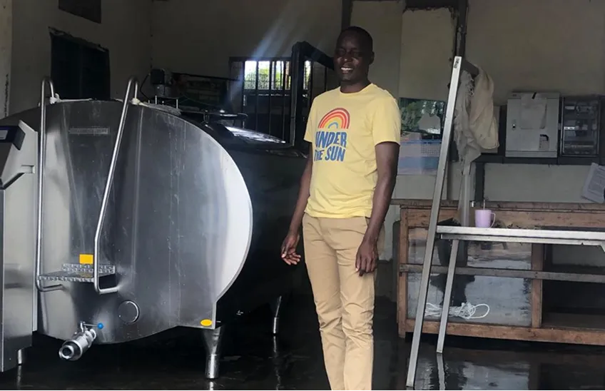 Man in a yellow 'Under the Sun' T-shirt standing next to a large stainless steel tank inside a room.