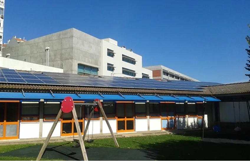 Building with solar panels on the roof and a playground swing set in front under blue sky.
