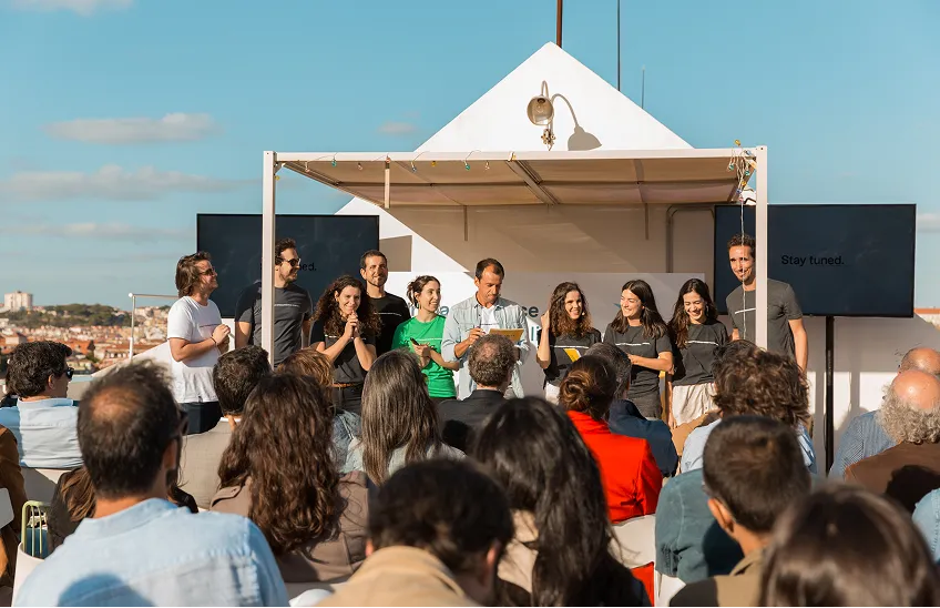 Group of people standing on a stage addressing an audience at an outdoor event on a sunny day.