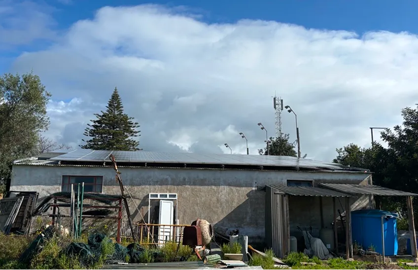 Flat roof building with solar panels, surrounded by various tools, equipment, and trees under a cloudy sky.