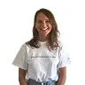 Smiling woman with wavy brown hair wearing a white t-shirt standing against a white background.