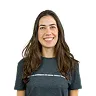 Smiling woman with long brown hair wearing a dark blue t-shirt against a white background.